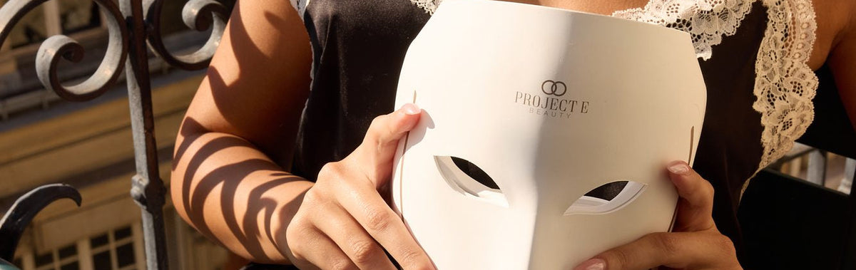 Close-up of a woman holding the white LumaLux Face V2 LED face mask at a balcony breakfast table