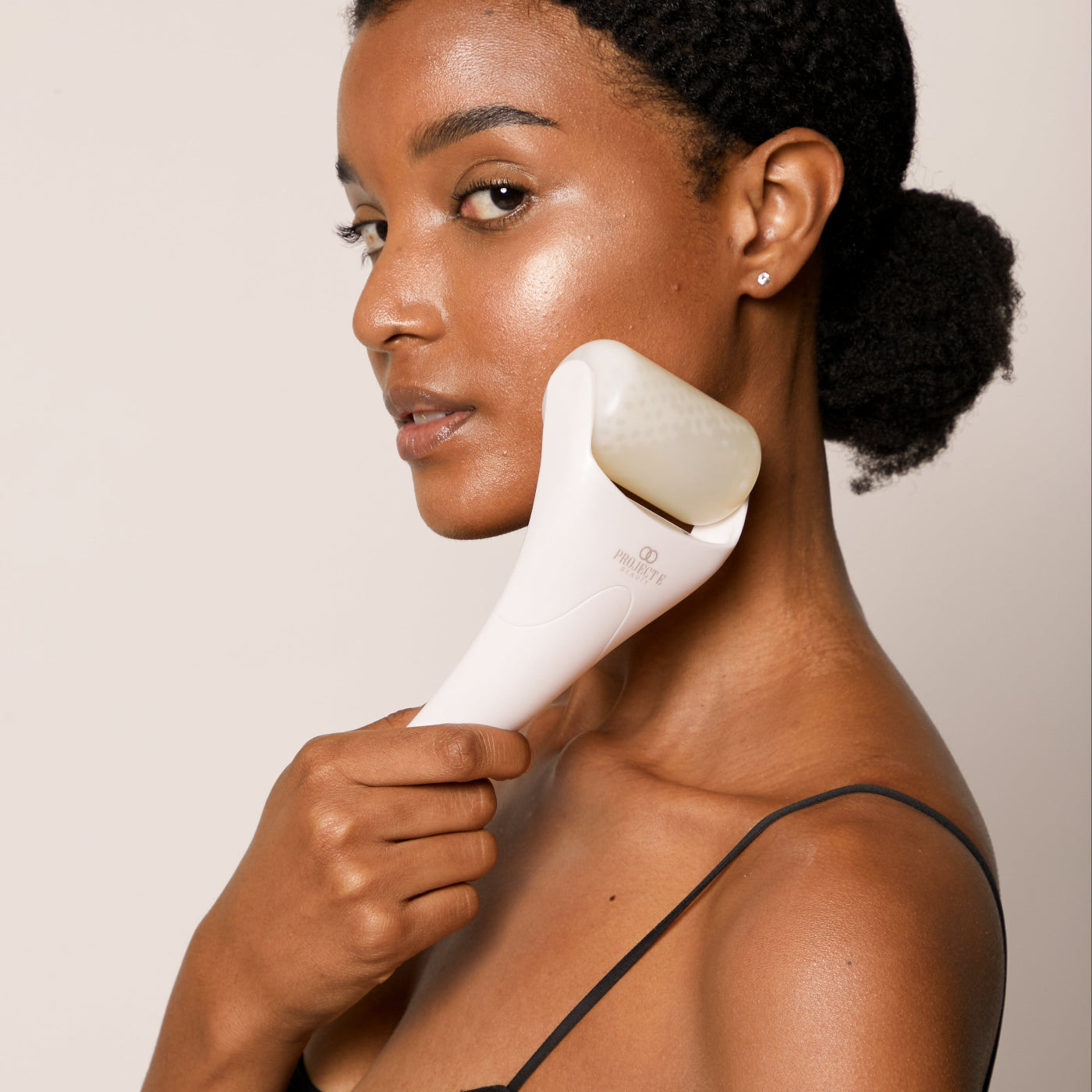 A model demonstrating the ergonomic white handle of the Project E Beauty Ice Roller on her cheek.