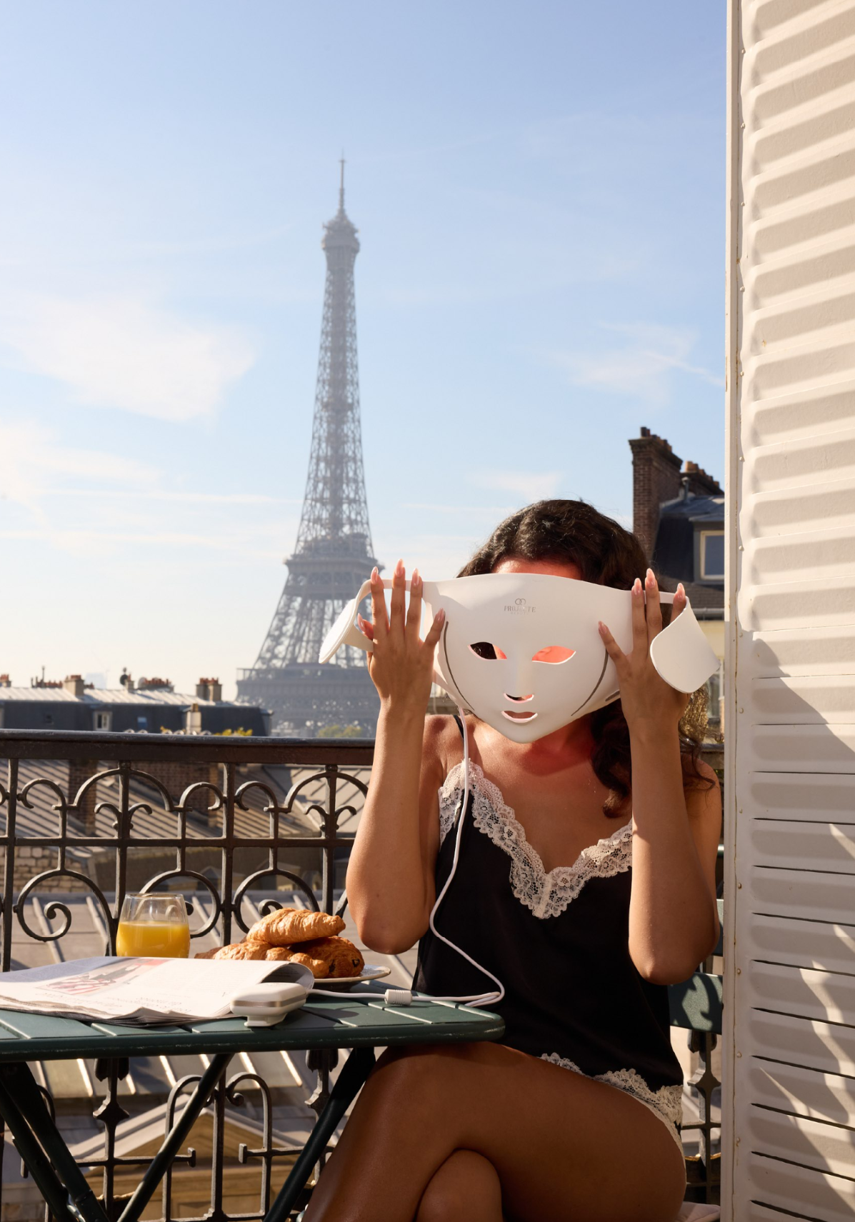 Woman holding the LumaLux Face V2 mask on a Paris balcony with the Eiffel Tower behind